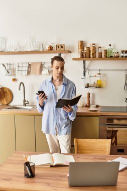 Zarif genç adam notları inceler ve telefonuna ışık dolu sıcak bir mutfakta bakar..