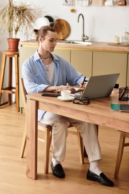 Genç, kadınsı bir adam sıcak bir mutfaktaki rahat bir masada dizüstü bilgisayarda yazı yazıyor..