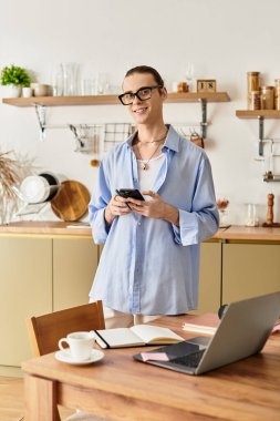 Kadınsı özellikleri olan genç bir adam şık bir mutfakta duruyor, telefonuyla meşgul..