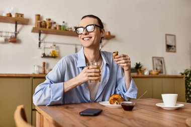 Genç yakışıklı bir adam sıcak bir mutfakta kruvasan ve meyve suyu içerken gülümsüyor..