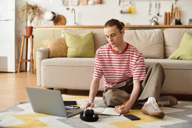 Dişi genç adam yerde oturur, rahat oturma odasından esinlenerek notlar yazar..