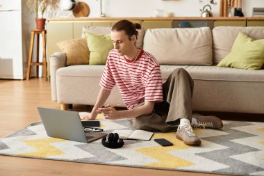 Genç ve yakışıklı bir adam dizüstü bilgisayarla çalışırken yerde dinleniyor..