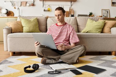 Genç bir adam yerde uzanıyor, rahat bir oturma odasında dizüstü bilgisayarında fikirleri keşfediyor..