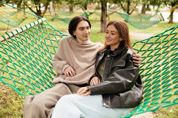 Young lovers share laughter and affection while relaxing in a cozy hammock surrounded by nature.