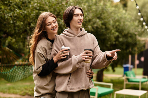A young couple shares a joyful moment outdoors, wrapped in warmth and laughter while holding coffee.