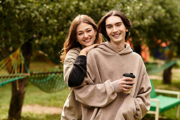 A joyful couple shares a tender moment outdoors, savoring coffee and laughter under green trees.
