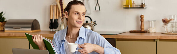 A youthful, handsome man sits in a modern kitchen, sipping tea and reading a book in tranquility.