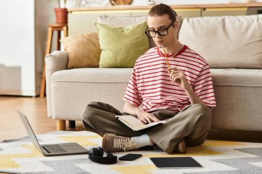 Kadınsı bir tarzı olan genç bir adam yerde oturur, defterine yazarken derin derin düşünür..
