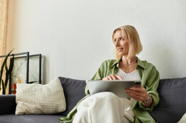 Evde dinlenen güzel bir kadın, yüzünde neşeli bir gülümsemeyle tabletinin tadını çıkarıyor..