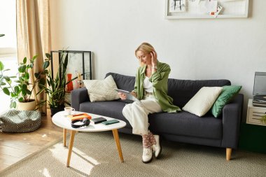 Güzel bir kadın kanepede dinlenir, rahat bir oturma odasında tabletine odaklanır..