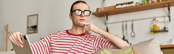 Женщина молодой человек сидит комфортно дома, потерявшись в мыслях, держа планшет.