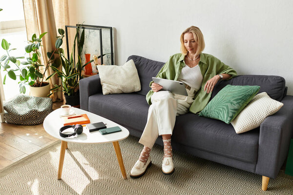 A beautiful woman enjoys her time at home reading on a tablet while sitting comfortably on a couch.