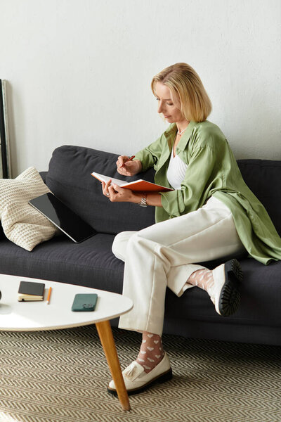 An adult woman sits comfortably on a couch, writing in a notebook with calm focus at her home.