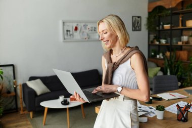 Hoş bir kadın rahat bir evde dizüstü bilgisayarını kullanırken gülümsüyor..