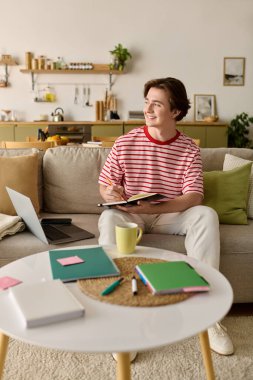 Odaklanmış genç bir adam evinde canlı bir öğrenim alanı ve kaynaklarla çevrimiçi çalışıyor..