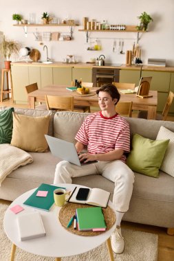 Genç bir adam modern dairesinde rahatça otururken çevrimiçi çalışmalarına odaklanıyor..