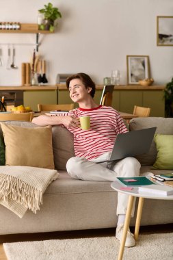 Genç bir adam şık dairesinde internetten ders çalışırken kanepede dinleniyor..