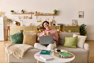 Genç adam, eğitim materyalleriyle çevrili, rahat ve modern evinden e-öğrenim görüyor..