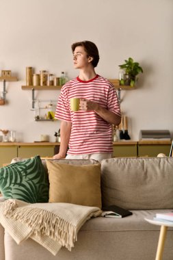 Genç bir adam dairesinde durmuş internetteki çalışmalarıyla meşgulken kahvesini yudumluyor..