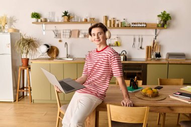 Genç bir adam, dizüstü bilgisayarıyla meşgul olarak şık dairesinden ders çalışıyor..