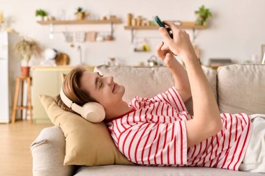 Genç bir adam evinde rahat rahat ders çalışıyor. Kanepede yatarken telefonunu kullanıyor..