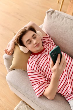 Genç adam kanepede uzanır, şık dairesinde dinlenirken internetten ders çalışır..