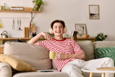 Genç bir adam kanepede rahatlar, bir dizüstü bilgisayar ve bir fincan sıcak kahveyle internetten ders çalışır..