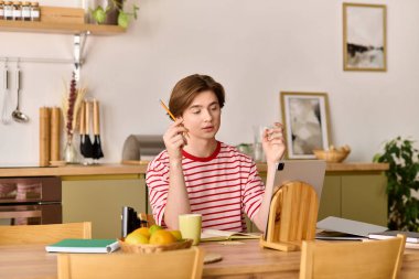 Genç bir adam modern bir dairede internetten ders çalışıyor, not alırken bilgisayarına odaklanıyor..