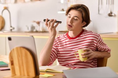 Genç bir adam rahat yerinde sıcak bir içki içerken dizüstü bilgisayar kullanarak evden ders çalışıyor..