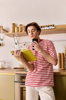 Genç bir adam modaya uygun mutfağında internetten ders çalışırken not alır..