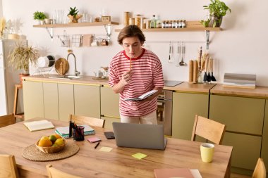 Genç bir adam şık dairesinde internetten ders çalışıyor, öğrenirken notlar alıyor..