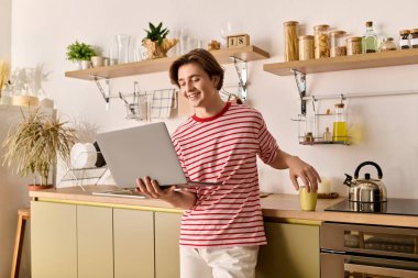 Genç bir adam internette öğrenim görüyor. Evde dizüstü bilgisayarıyla çalışırken gülümsüyor..