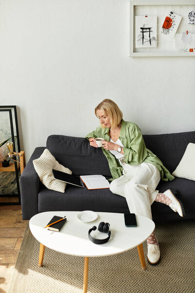 Beautiful woman relaxes at home, sipping tea and reading on a cozy sofa in casual outfit.