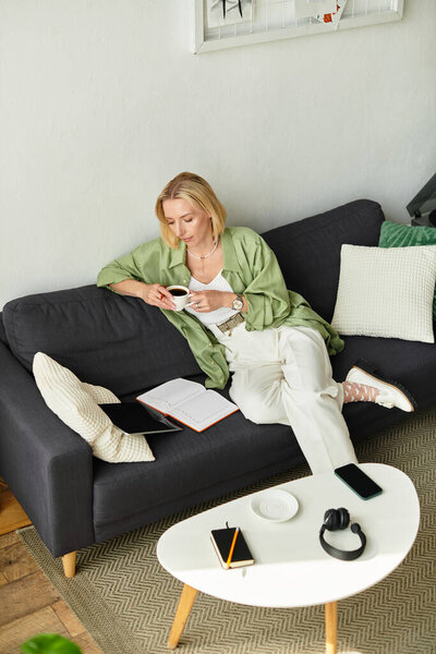 Beautiful woman enjoys a warm drink while lounging at home in casual attire, surrounded by comfort.