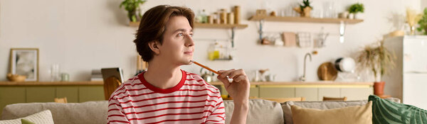 Молодой человек учится онлайн в своей уютной квартире, глубоко в мыслях с карандашом в руке, баннер