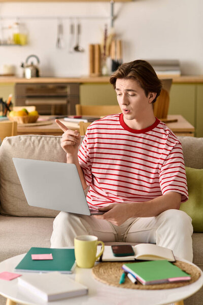 Студент использует свой ноутбук, чтобы учиться в Интернете, сидя комфортно в своей стильной квартире.