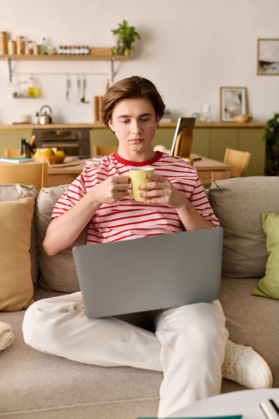 Молодой человек удобно сидит дома, учится онлайн с ноутбуком и горячим напитком.