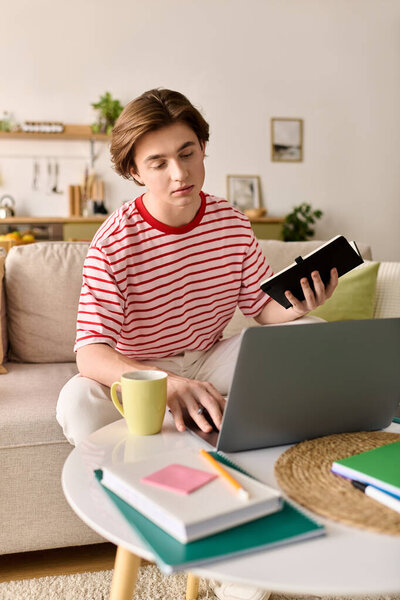 Молодой человек сидит дома, учится онлайн со своим ноутбуком, потягивая кофе и читая заметки.