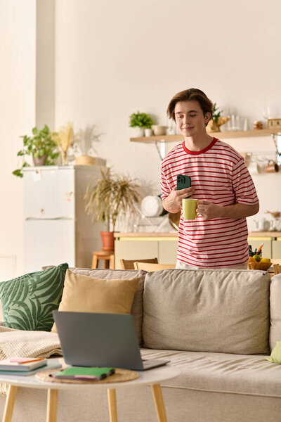 A young man enjoys studying online in a cozy modern apartment while sipping coffee.