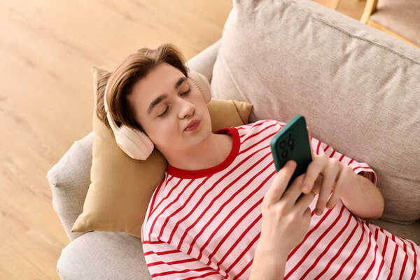 Молодой человек расслабляется на диване, используя наушники и телефон для онлайн-занятий.