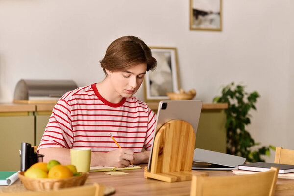 A young man is studying online at his modern apartment, focused on his work with a laptop.