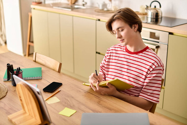 A young man in striped shirt is studying online from his stylish apartment, taking notes.