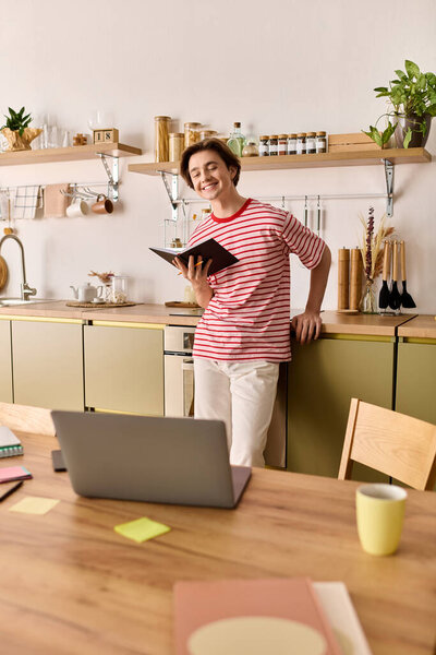 Молодой человек учится онлайн в своей уютной современной квартире, улыбаясь и держа в руках блокнот.