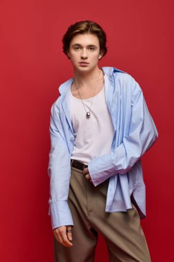 Genç bir adam kendine güveni tam mavi bir gömlek ve pantolonla kırmızı bir fona karşı poz veriyor..