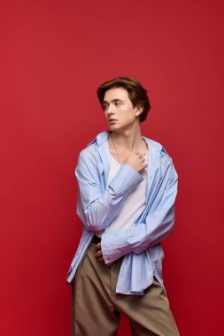 Şık mavi gömlekli ve pantolonlu kendine güvenen genç bir adam, parlak kırmızı bir arka plana karşı..