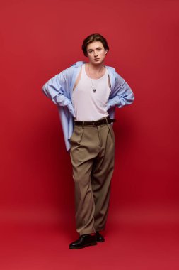 Şık bir genç adam kendine güvenerek poz verir ve kırmızı arka planda mavi bir gömlek giyer..