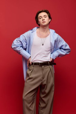 Şık bir genç adam, kendine güvenen mavi gömlekli ve pantolonlu bir şekilde poz verir. Moda atmosferi yayar..