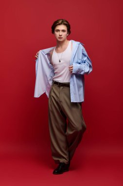 Modaya uygun genç bir adam kendine güvenerek şık bir elbiseyle poz veriyor. Üzerinde pantolon ve mavi gömlek var.