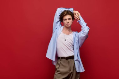 Şık bir genç adam kendine güvenerek poz veriyor. Şık pantolonlar ve modern yetenekler saçan mavi bir gömlek..