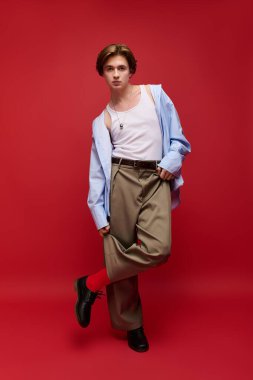 Şık bir genç adam, koyu kırmızı bir arka plana karşı, modaya uygun bir şekilde poz veriyor..